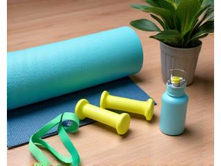 A home gym setup with a yoga mat, resistance bands, light dumbbells, and a foam roller neatly arranged on a wooden floor, suggesting fitness and recovery.